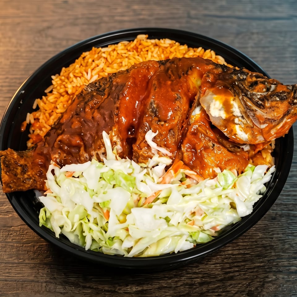 Whole fried fish covered in red sauce, served with rice and coleslaw in a black bowl.