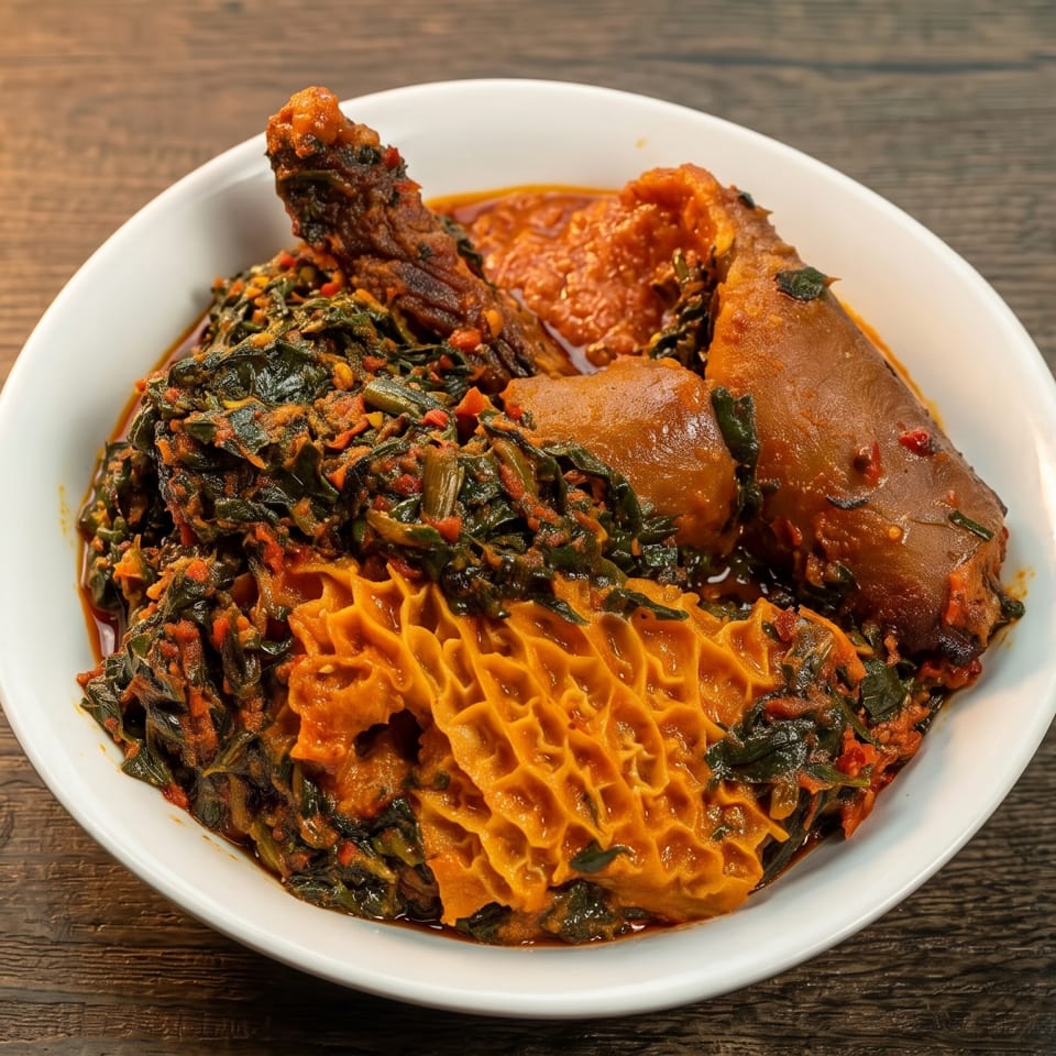 A white bowl filled with a rich, dark green stew, tripe, and meat on a wooden table.