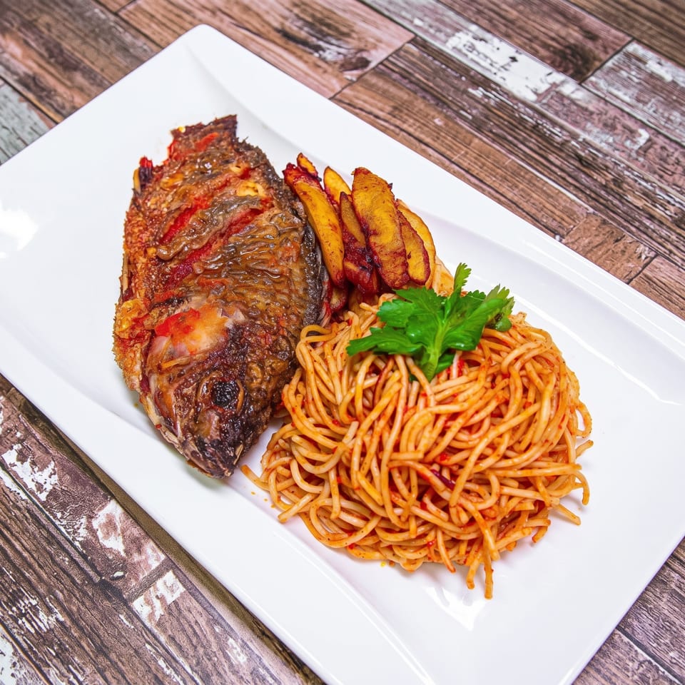 Fried whole fish, plantains, and spaghetti with sauce and cilantro on a white plate.