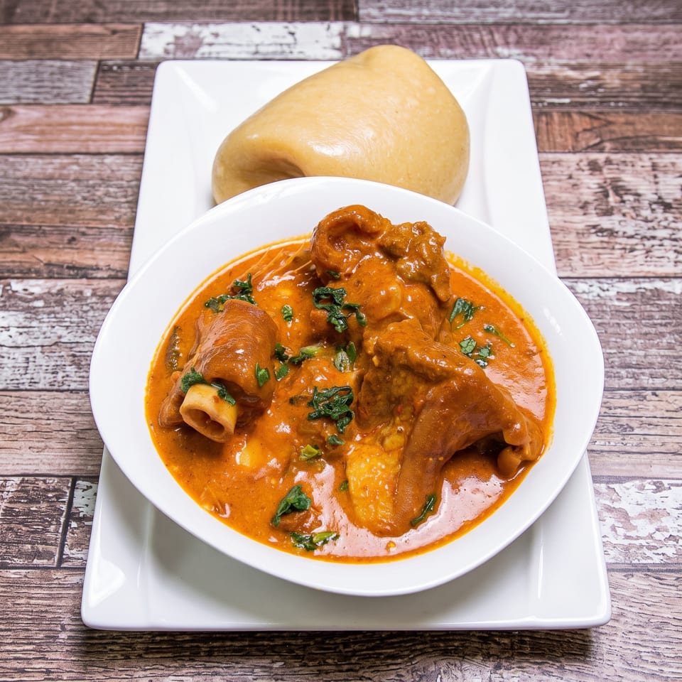 A bowl of rich, orange stew with meat and greens, served with a side of fufu.